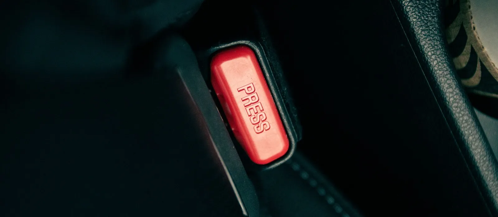Seat belt buckle with a red press button in a dark vehicle interior