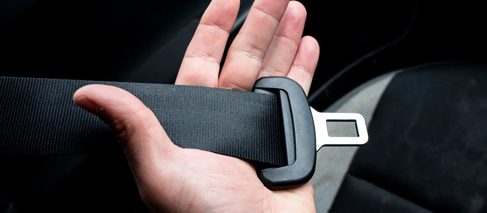 A hand holding a seat belt latch plate inside a vehicle
